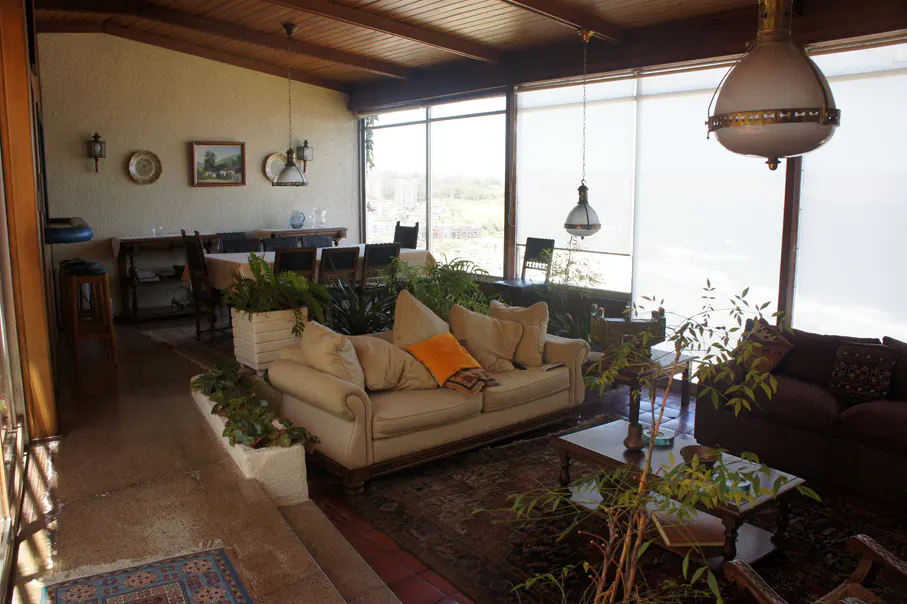 Living room with beige sofa, brown sofa, plants, dining table, and large windows with a view.
