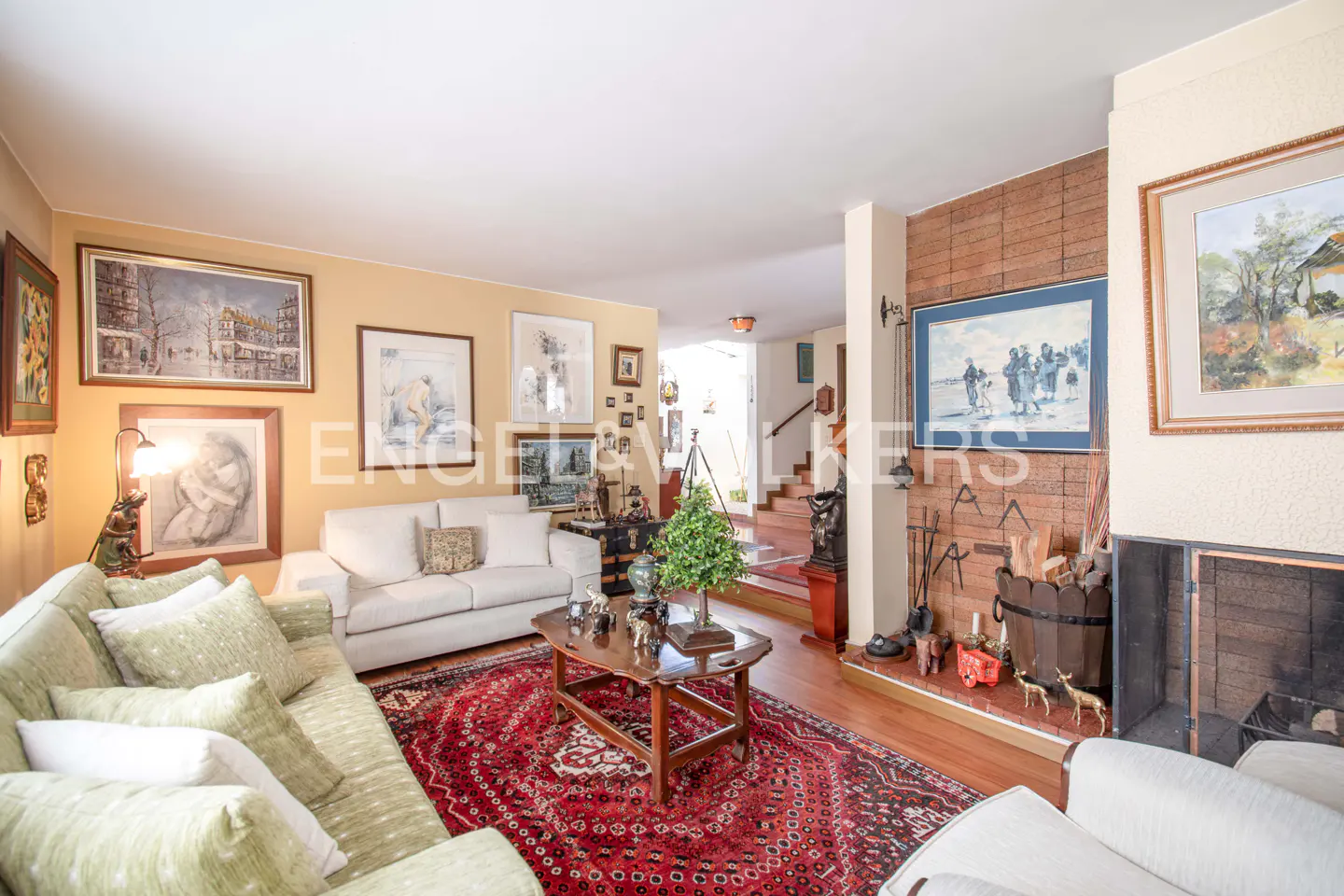 Living room with a green sofa, white sofa, red rug, fireplace, and many framed pictures on the wall.