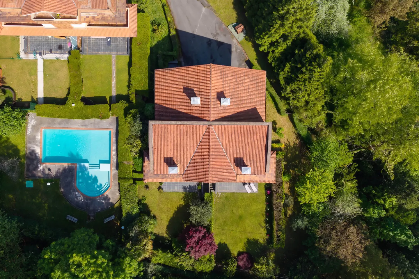 Aerial view of a house with a red tile roof, a blue swimming pool, and green lawns surrounded by trees.