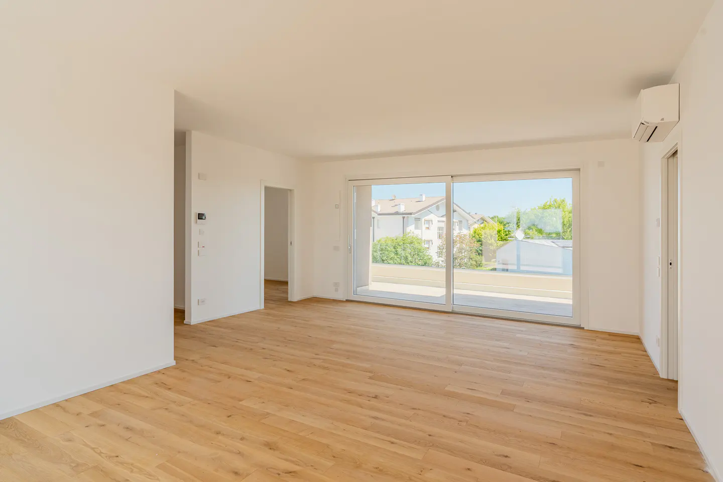Bright, empty room with light wood floors, white walls, and a large sliding glass door to a balcony.