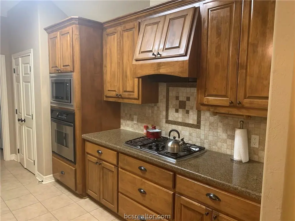 Kitchen with medium-toned wood cabinets, granite countertops, stainless steel appliances, and a tiled backsplash.