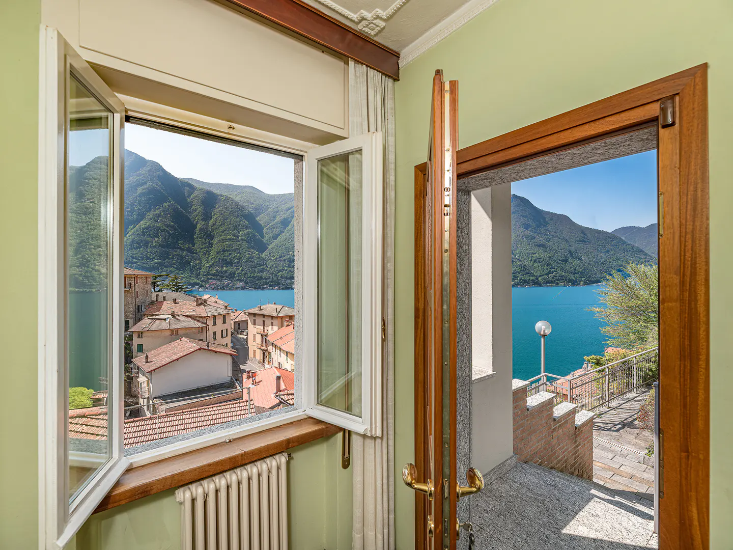 Interior view with open window showing a town and lake, and open door to a patio with lake view.