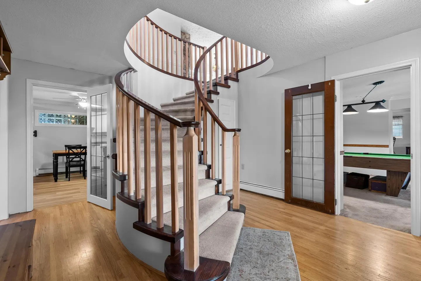 Foyer with a curved staircase, light wood floors, and white walls. A pool table is visible through an open door.