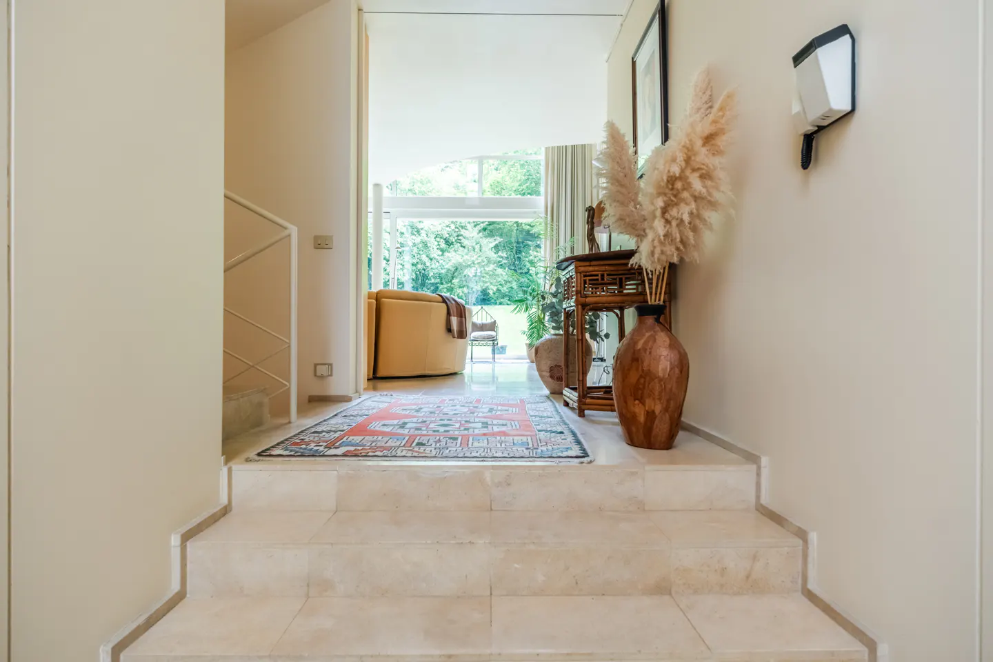 Interior view of a home with marble stairs leading to a living room with a rug, chair, and outdoor view.