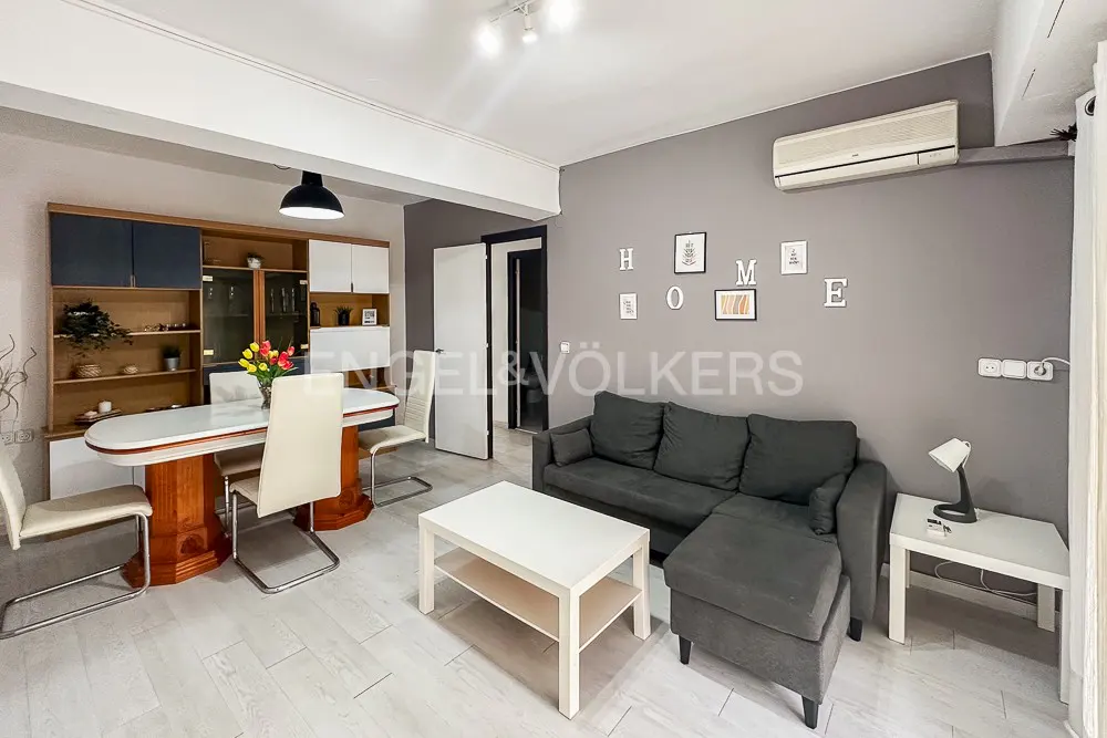 Living and dining area with gray walls, light wood floors, and modern furniture. A gray sofa faces a white coffee table. "HOME" decorates the wall.
