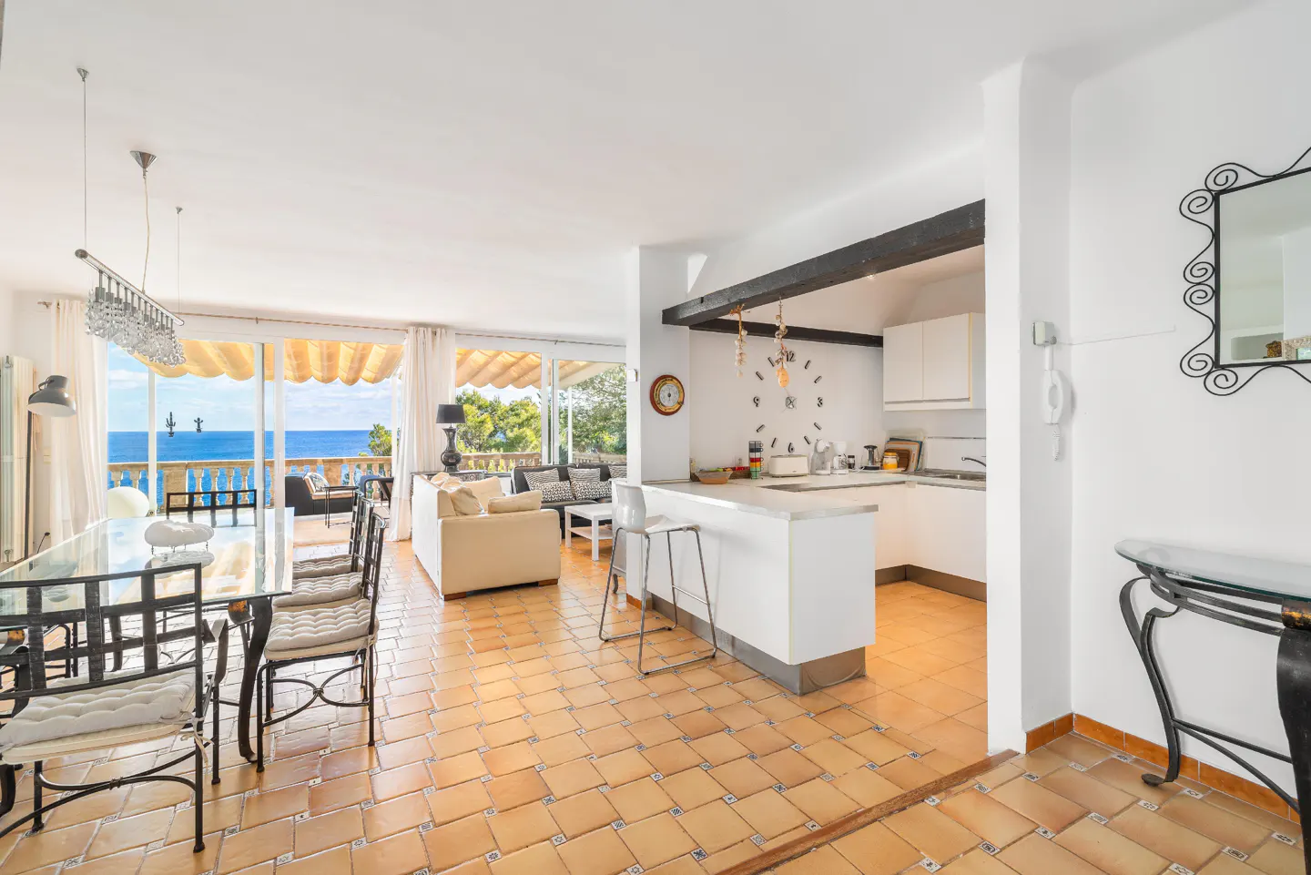 Open-concept living space with dining table, white sofa, kitchen with island, and ocean view through large windows.
