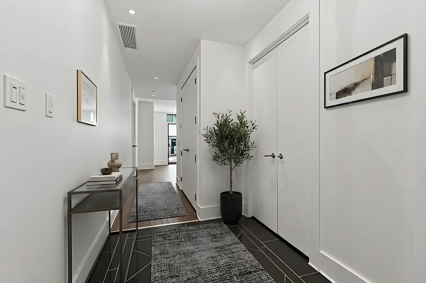 Hallway with white walls, black tile floor, console table, plant, and artwork.