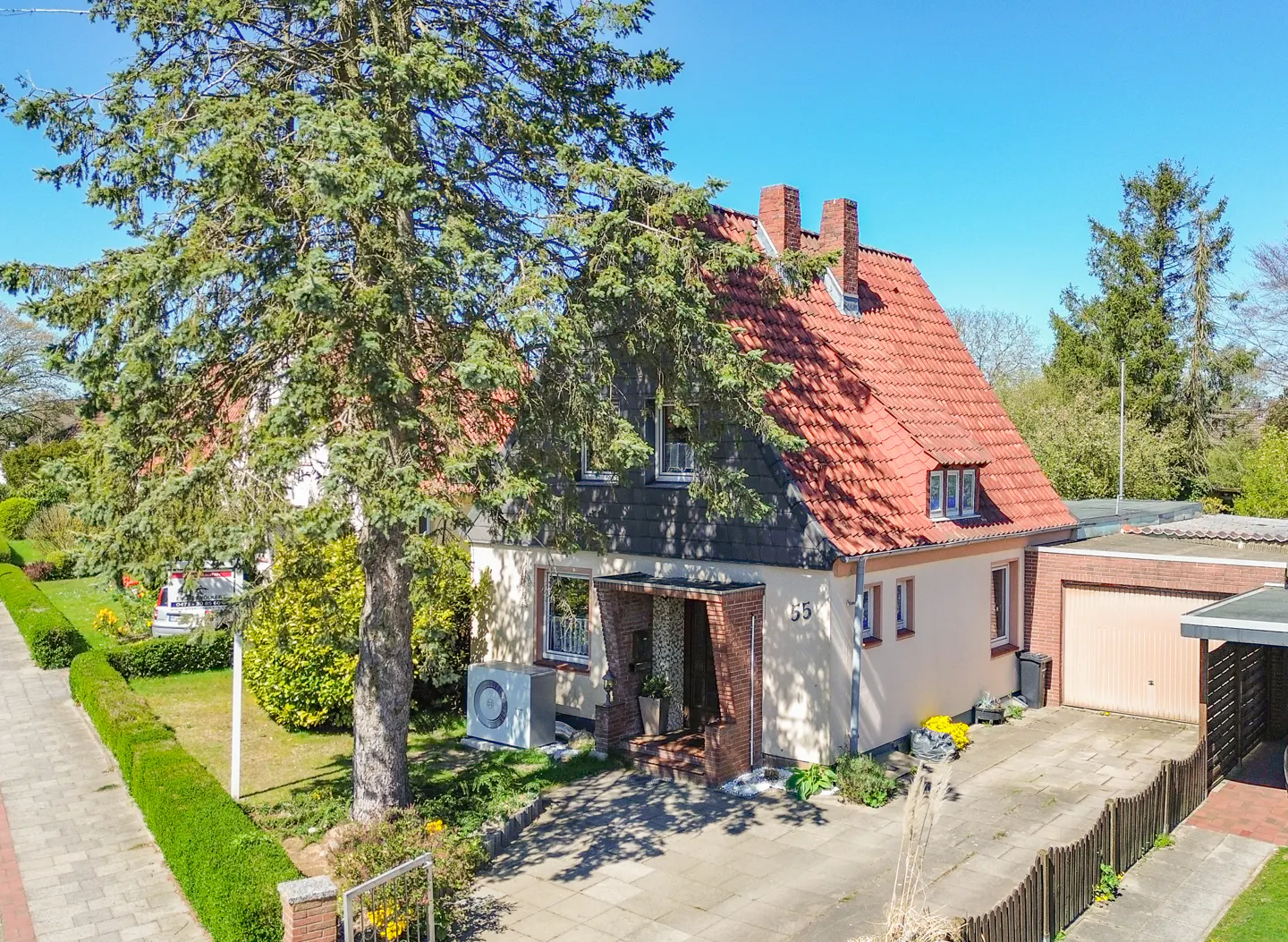 Two-story house with a red tile roof and a large tree in the front yard on a sunny day.