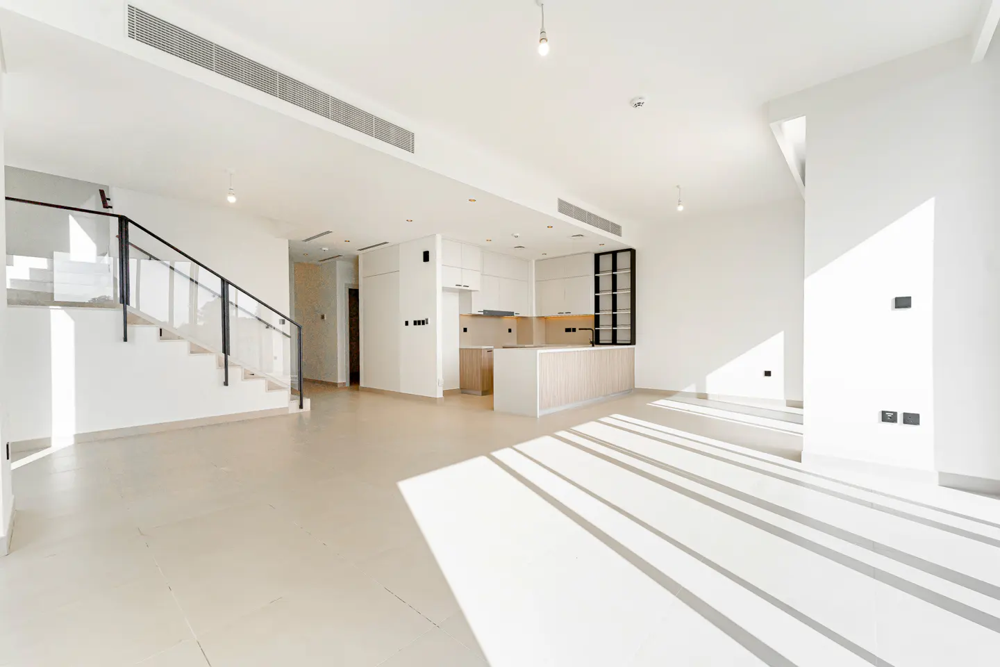 Bright, modern open-plan living area with a white kitchen, light wood accents, and a staircase with a black railing.