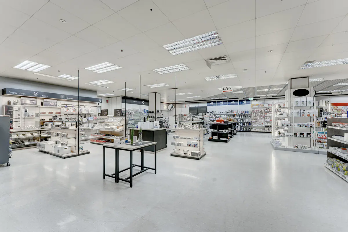 A bright, spacious retail store with white floors and shelves displaying various kitchen and home goods.