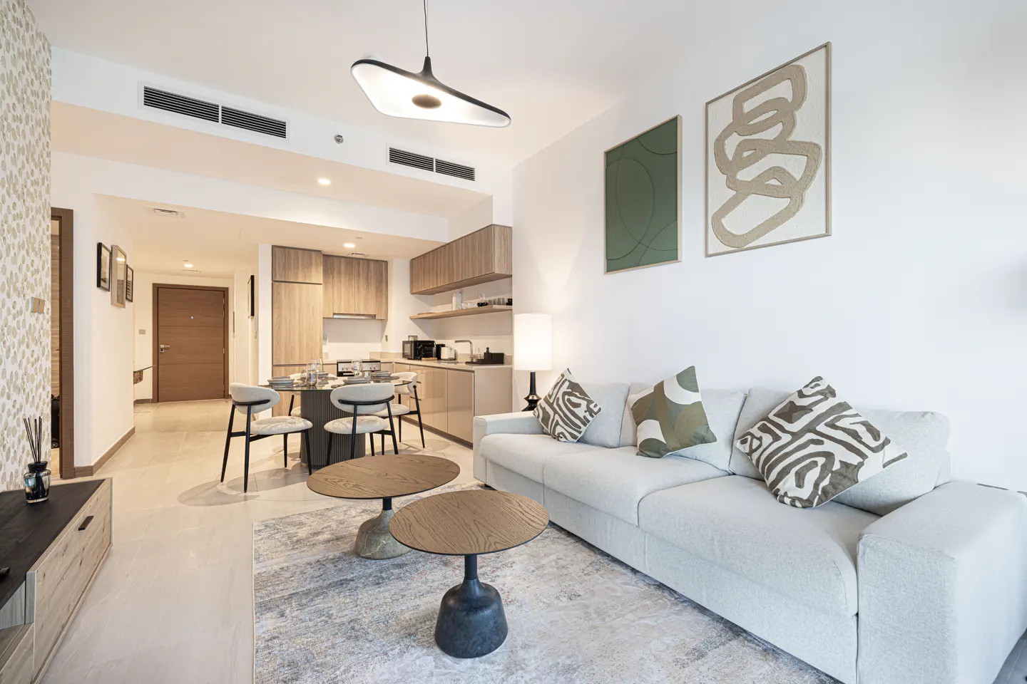Bright apartment interior with a white sofa, round tables, and a kitchen with a dining area in the background.