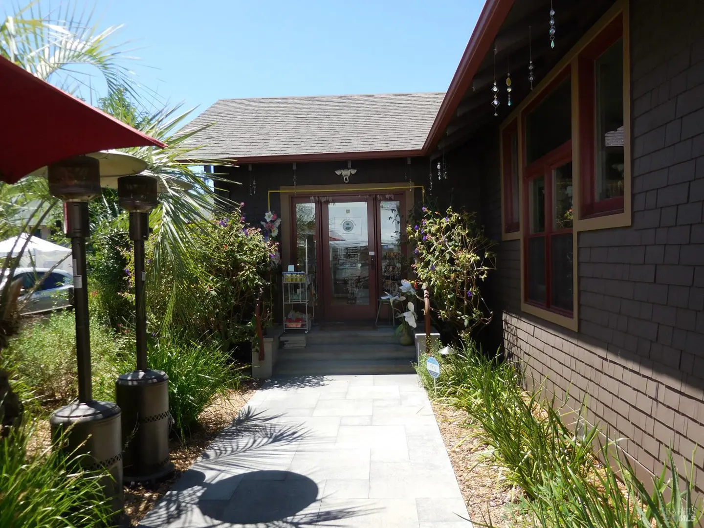 Exterior view of a brown building with red trim, a gray stone walkway, and lush green landscaping.