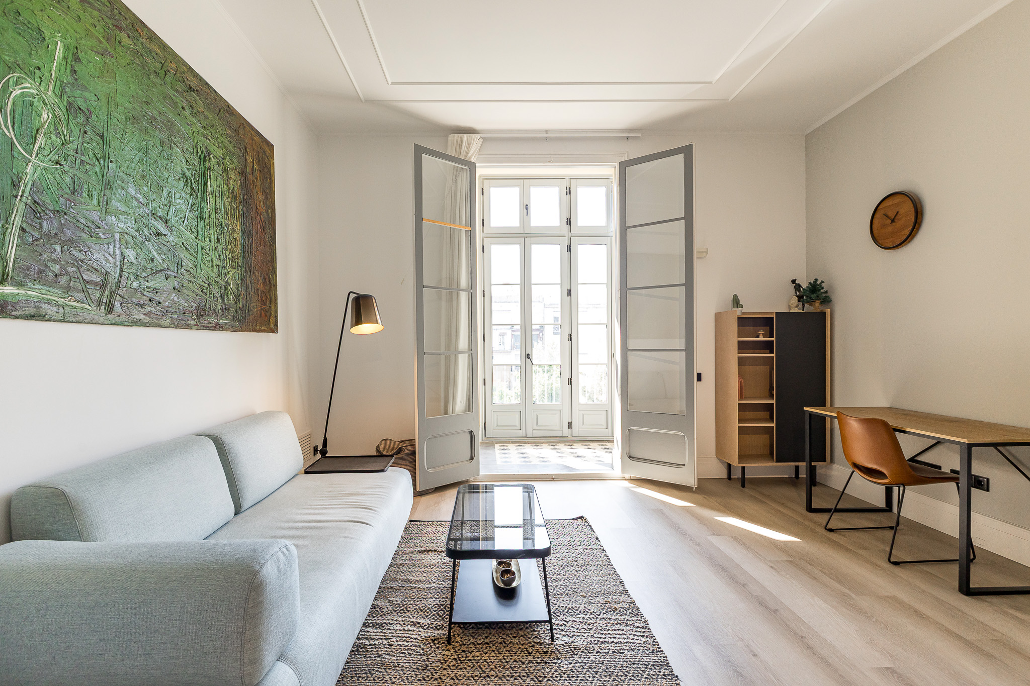 Modern living room with a light blue sofa, glass coffee table, desk, and large green abstract painting on a white wall. [AI-generated text]