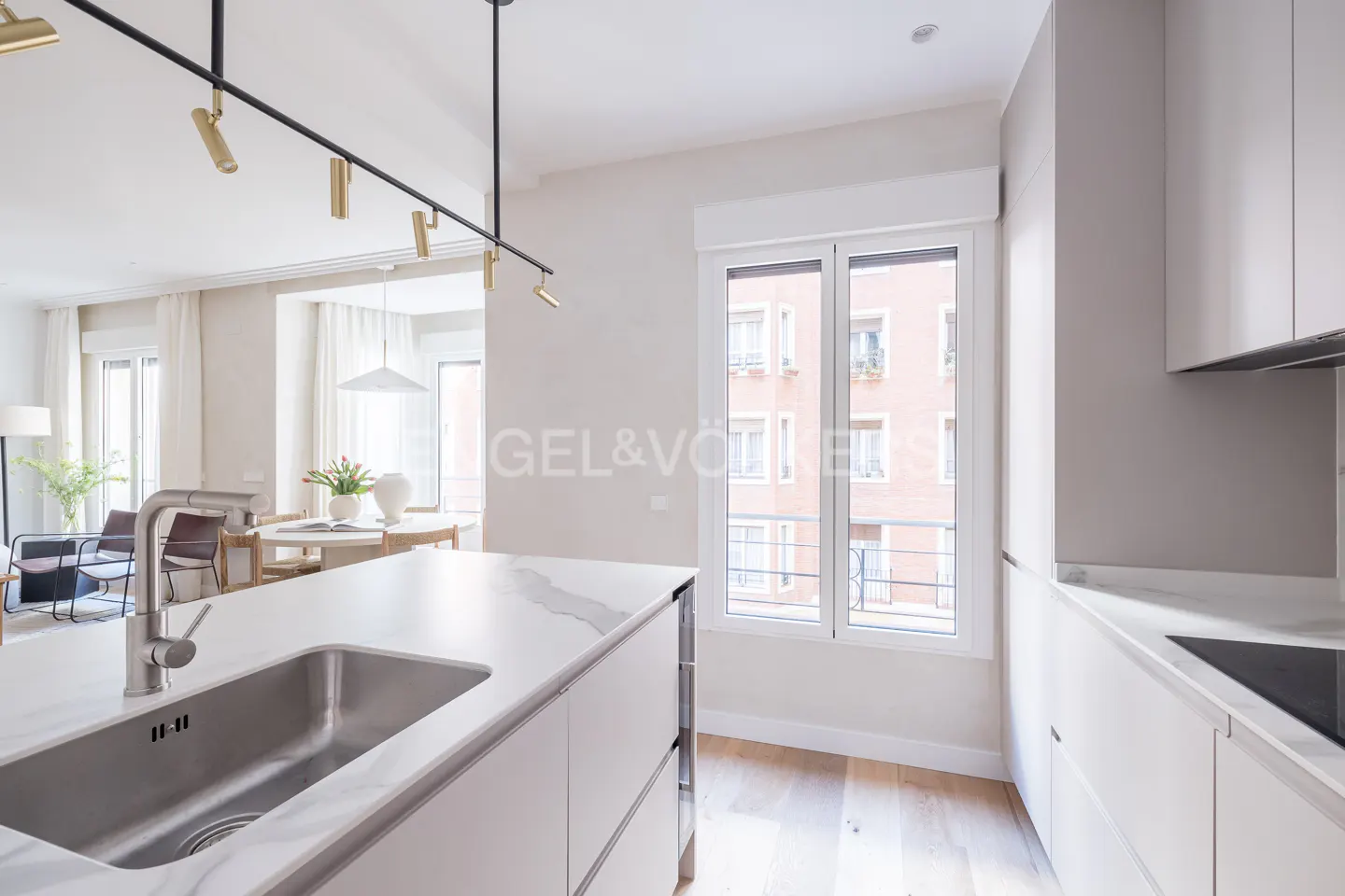 Modern kitchen with white marble island, stainless steel sink, and sleek cabinets, overlooking a bright dining area.
