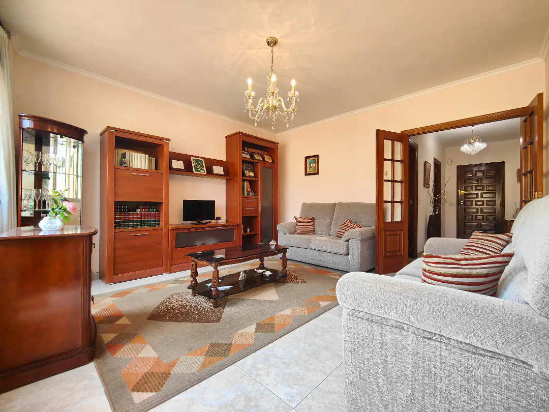 Living room with light walls, grey sofas, wooden furniture, a patterned rug, and a crystal chandelier.