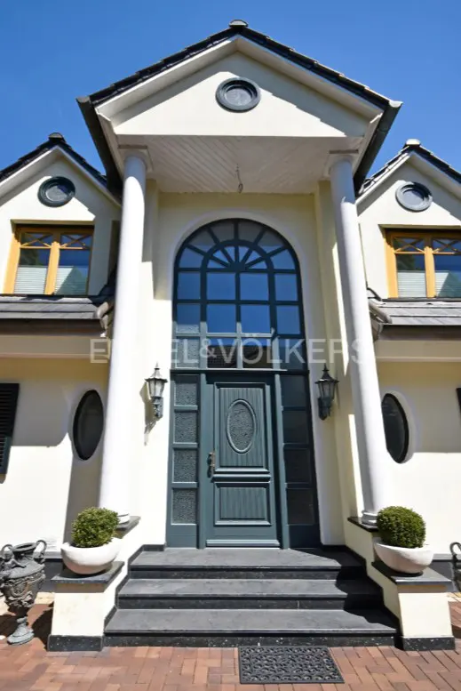 Front view of a two-story house with a blue door, white columns, and black steps leading up to the entrance.