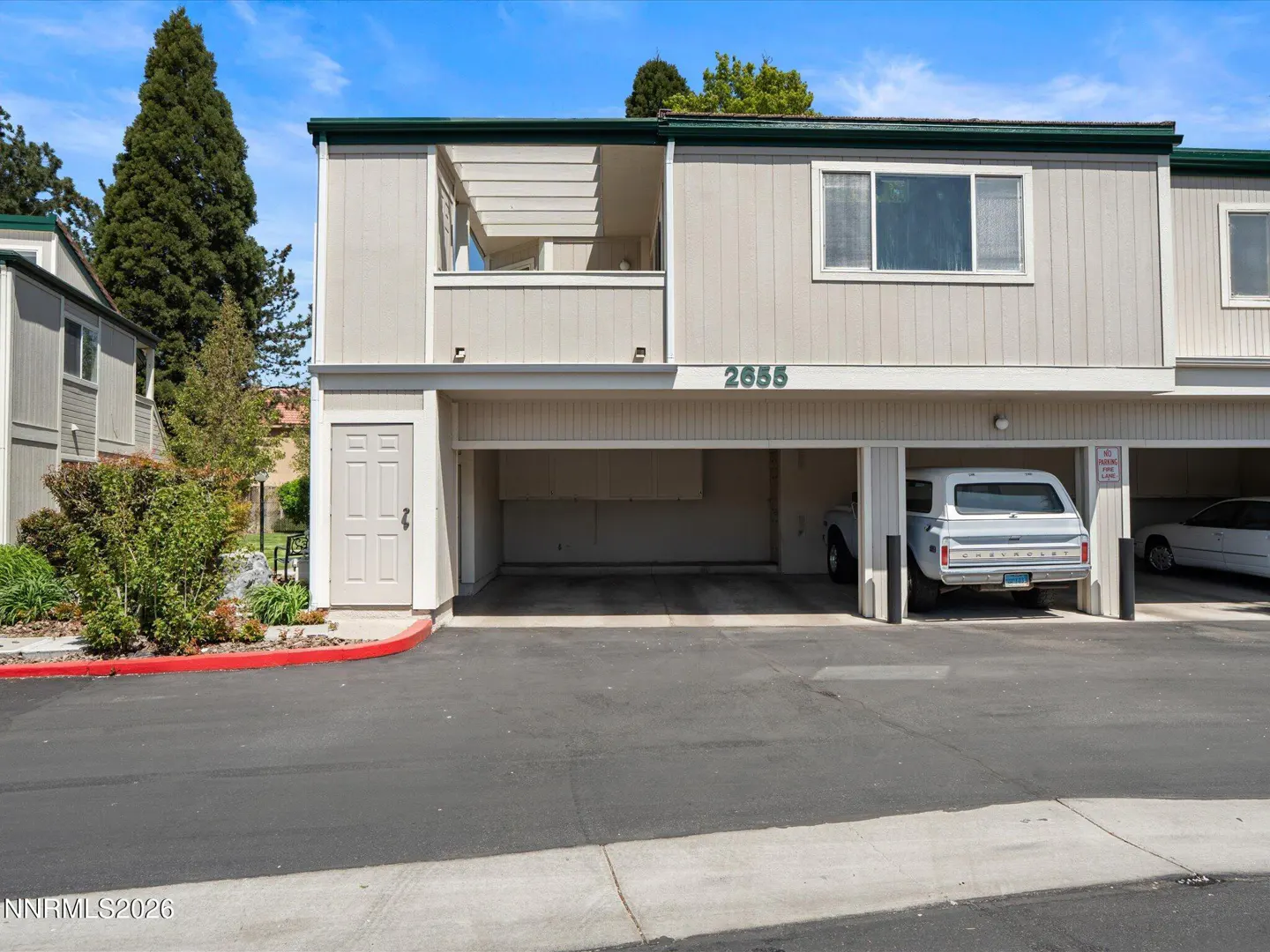 Exterior view of a two-story, light-grey townhouse with open carports and a white SUV parked inside. The address "2655" is visible above the carport.