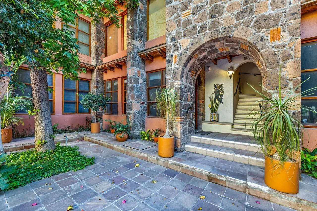 Courtyard view of a stone building with an arched entrance, potted plants, and a tiled patio.