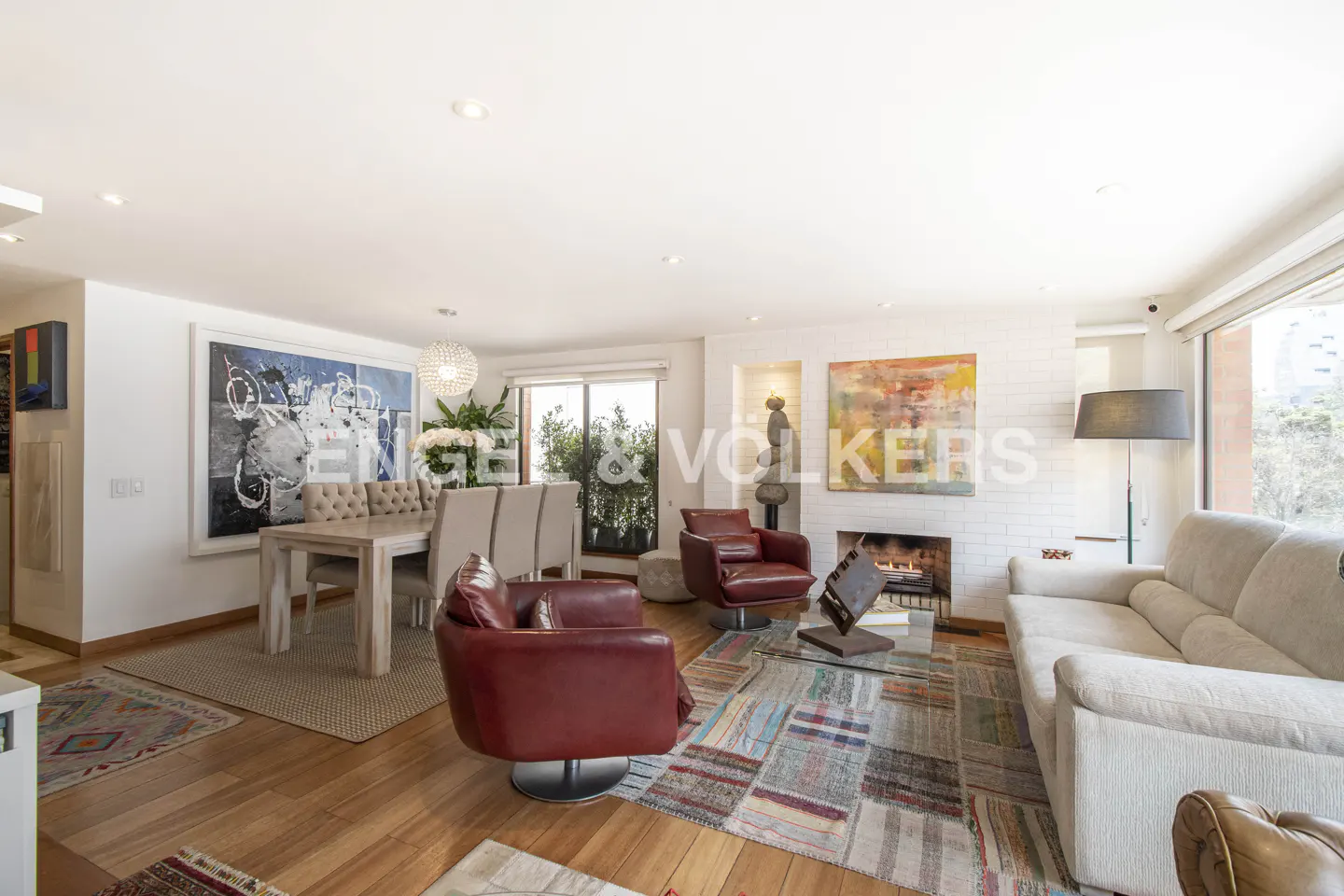 Bright living and dining room with white walls, hardwood floors, red leather chairs, a white sofa, and a fireplace.