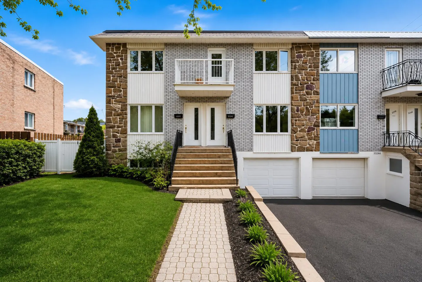 Exterior of a two-story townhouse with stone and brick facade, white trim, and a small balcony above the front door. A paved walkway leads to the entrance.