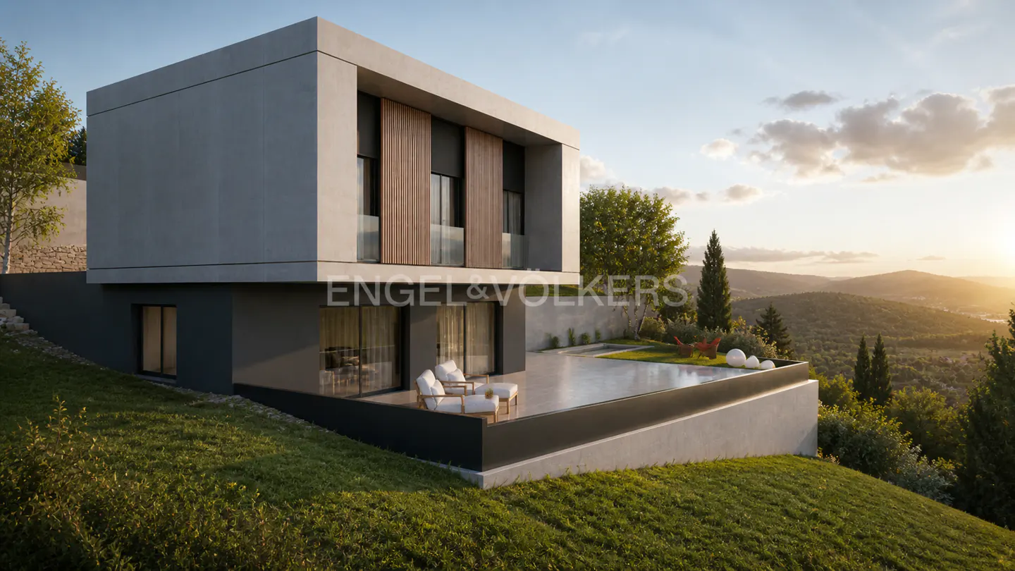 Modern two-story gray house on a green hillside with a patio and mountain views at sunset.