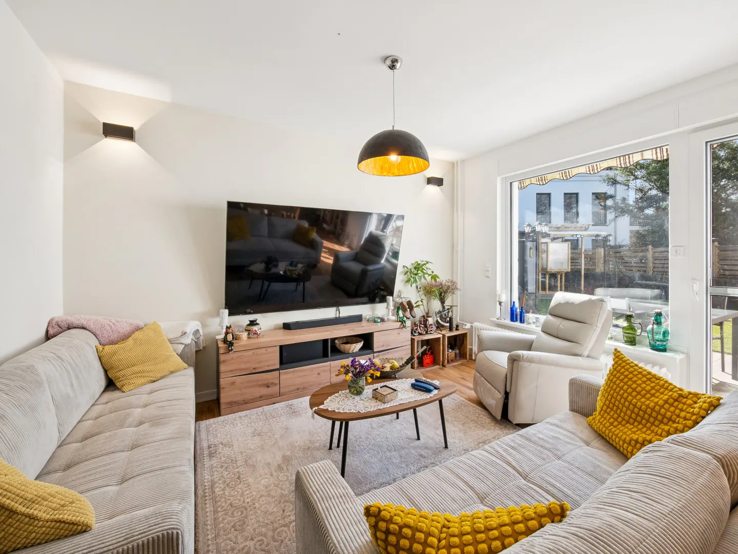 Bright living room with two gray sofas, yellow pillows, a wooden TV stand, and a large window.