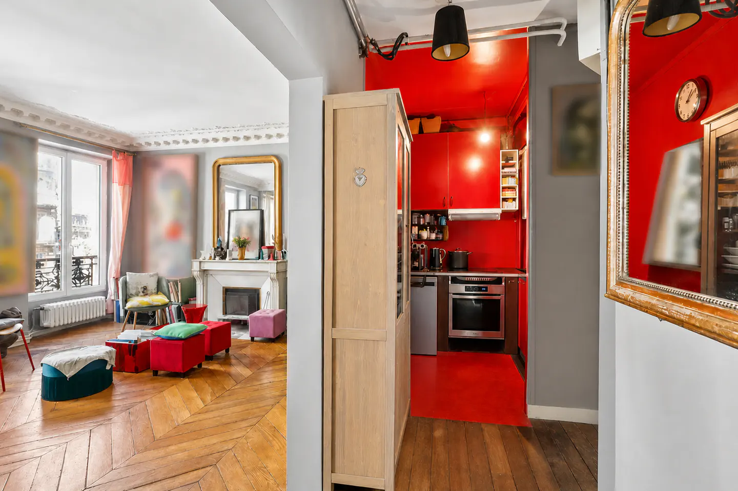 A view into a Parisian apartment with a red kitchen, wooden floors, and a living room with a fireplace.