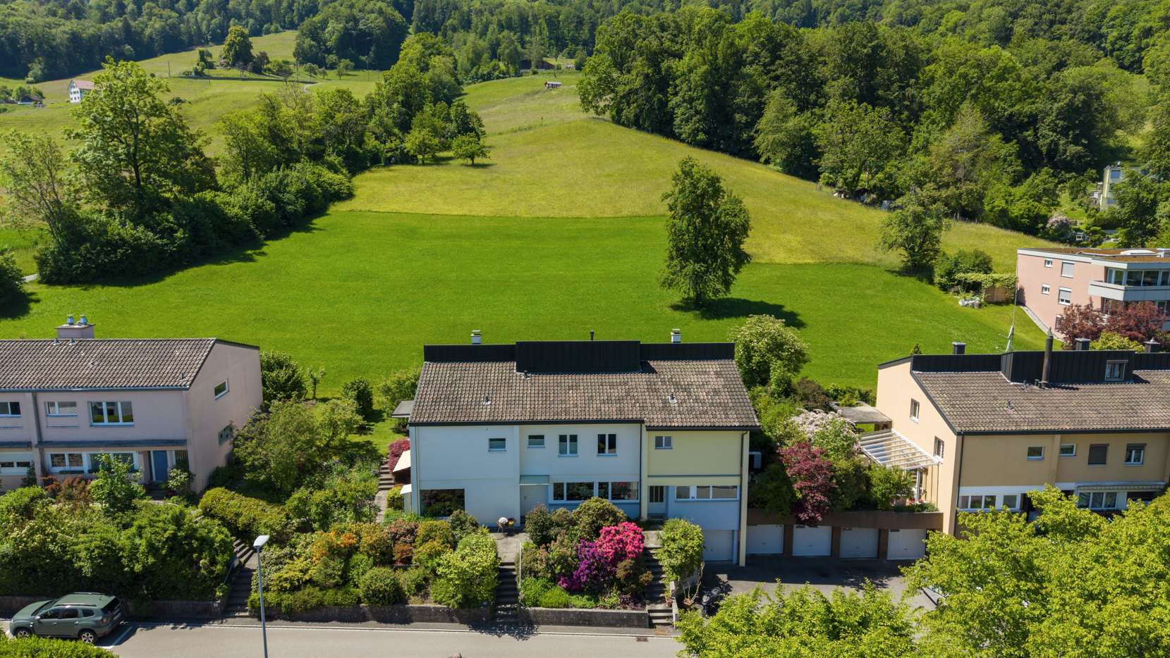 Aerial view of a multi-family home with a lush green hillside in the background on a sunny day.