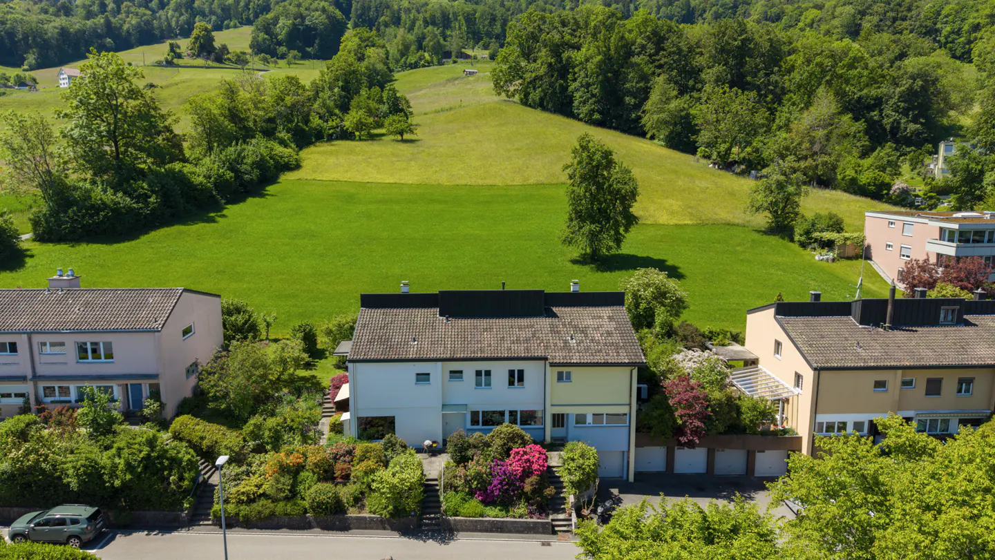 Aerial view of a multi-family home with a lush green hillside in the background on a sunny day.