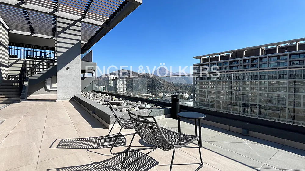 Rooftop patio with two chairs, a small table, and a view of mountains and buildings under a blue sky.