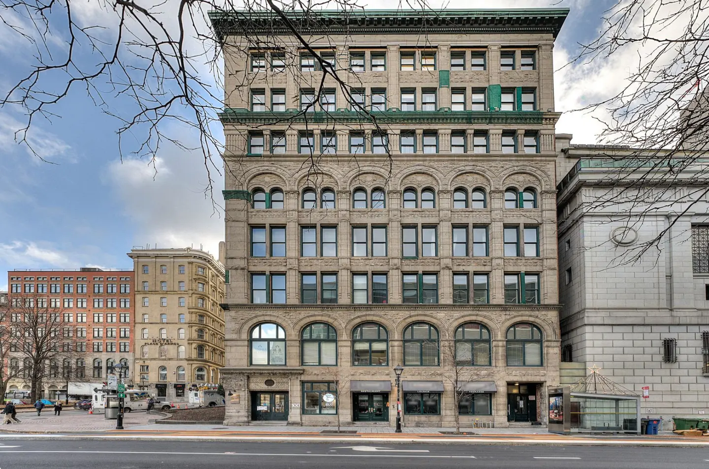 Exterior view of a tall, tan brick building with green window frames and arched windows on the lower floors.