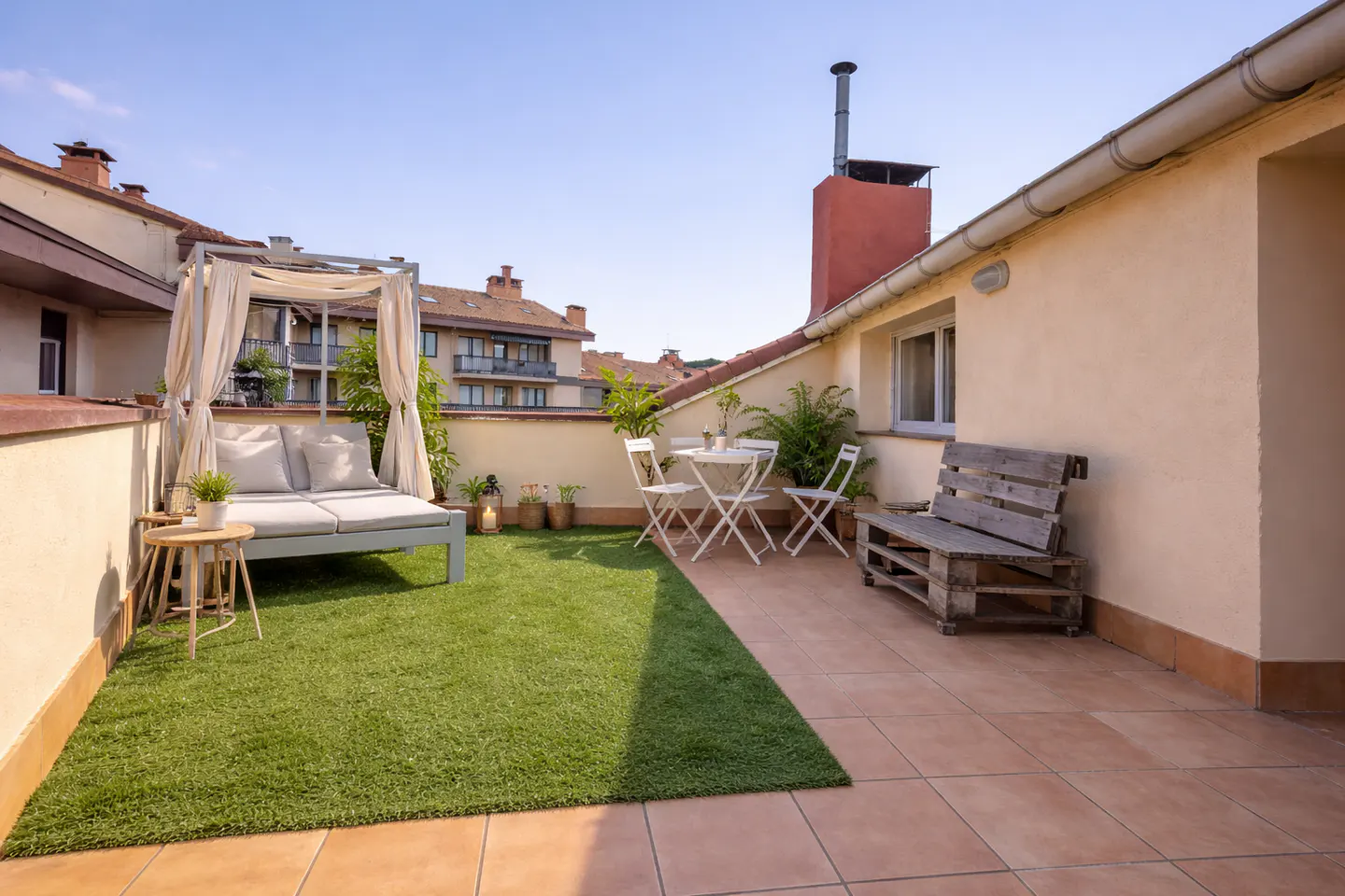 Rooftop patio with artificial grass, a daybed with white curtains, a white table with chairs, and a wooden bench.