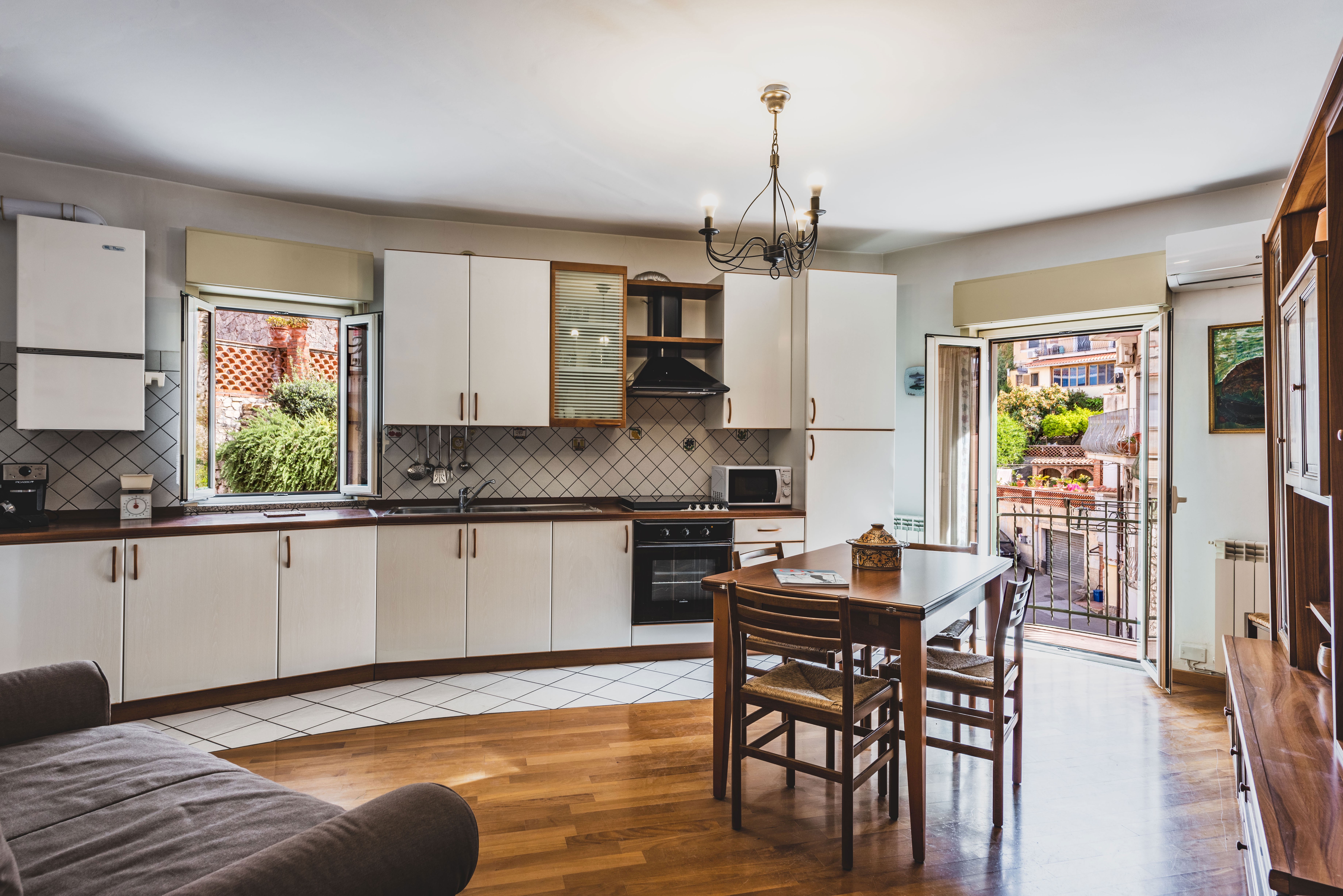Bright kitchen with white cabinets, wooden floors, a dining table, and open doors leading to a balcony.