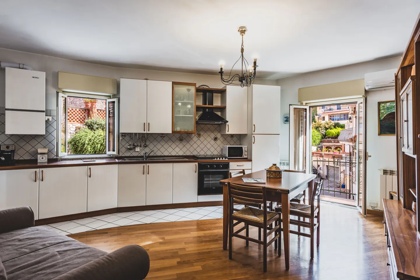Bright kitchen with white cabinets, wooden floors, a dining table, and open doors leading to a balcony.