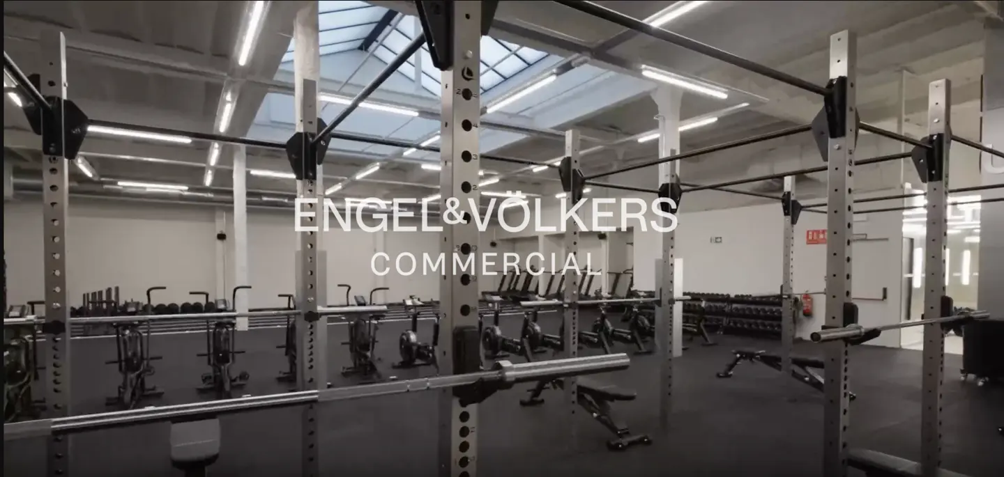 Gym interior with squat racks, exercise bikes, and weights. Engel & Volkers Commercial logo overlay.