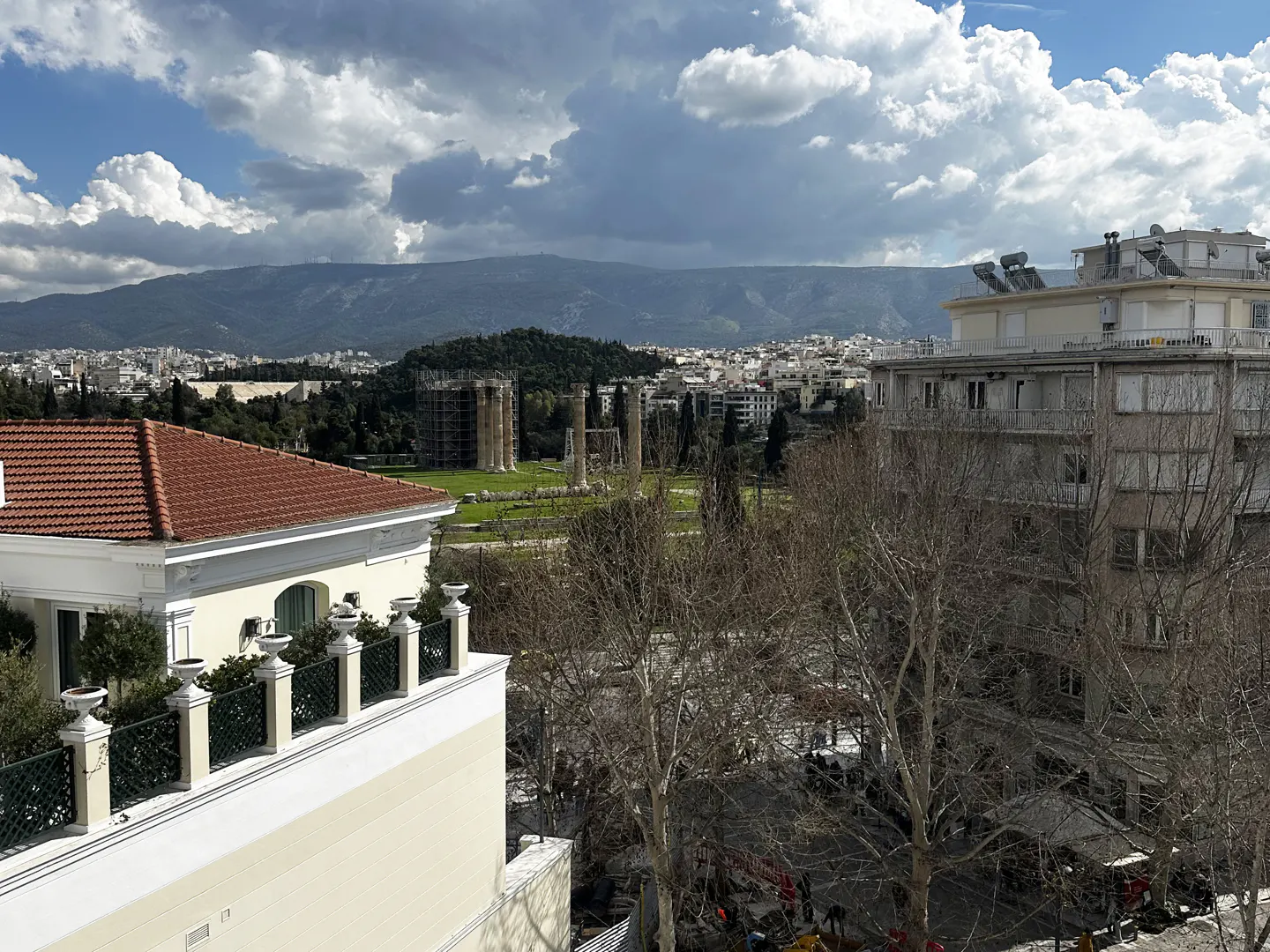 View of Athens, Greece, with the Temple of Olympian Zeus ruins in the distance. Buildings and bare trees are in the foreground.