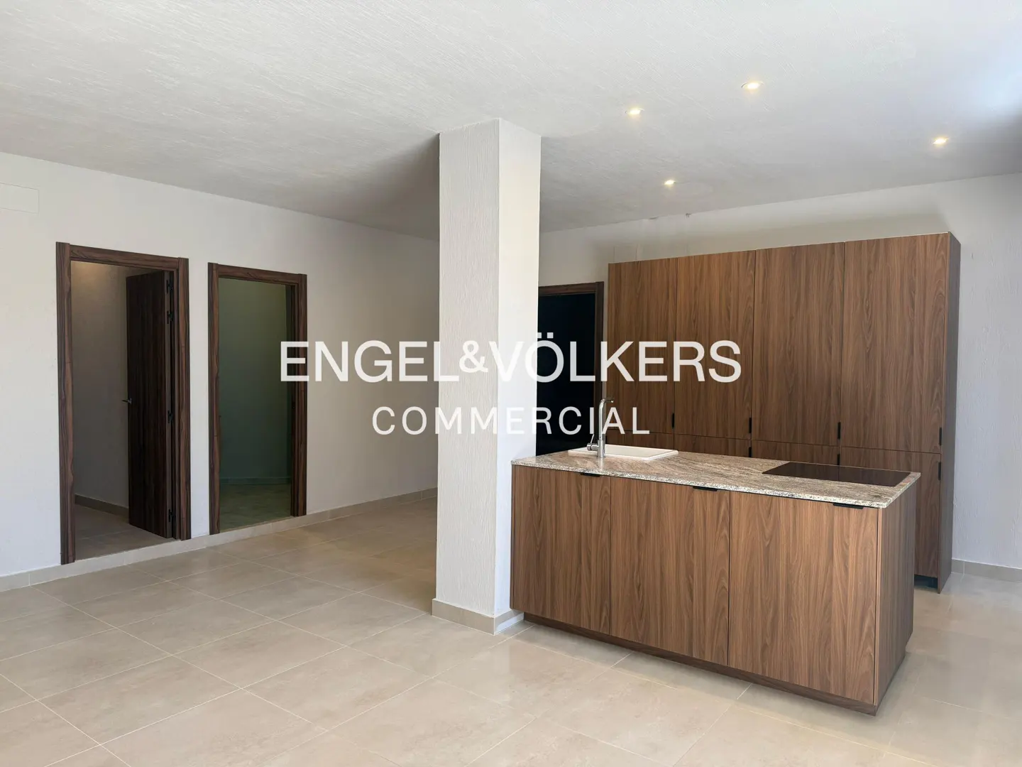 A modern kitchen with wood cabinets, a granite countertop island, and two open doorways. The floor is tiled in a light beige color.