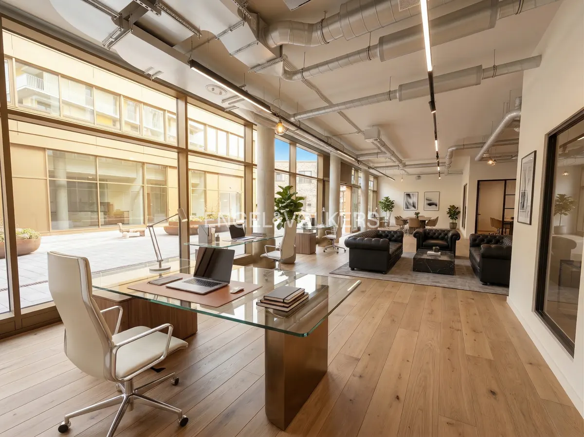 Bright, modern office space with wood floors, exposed ductwork, and large windows overlooking a courtyard. Desks, chairs, and black leather sofas furnish the area.