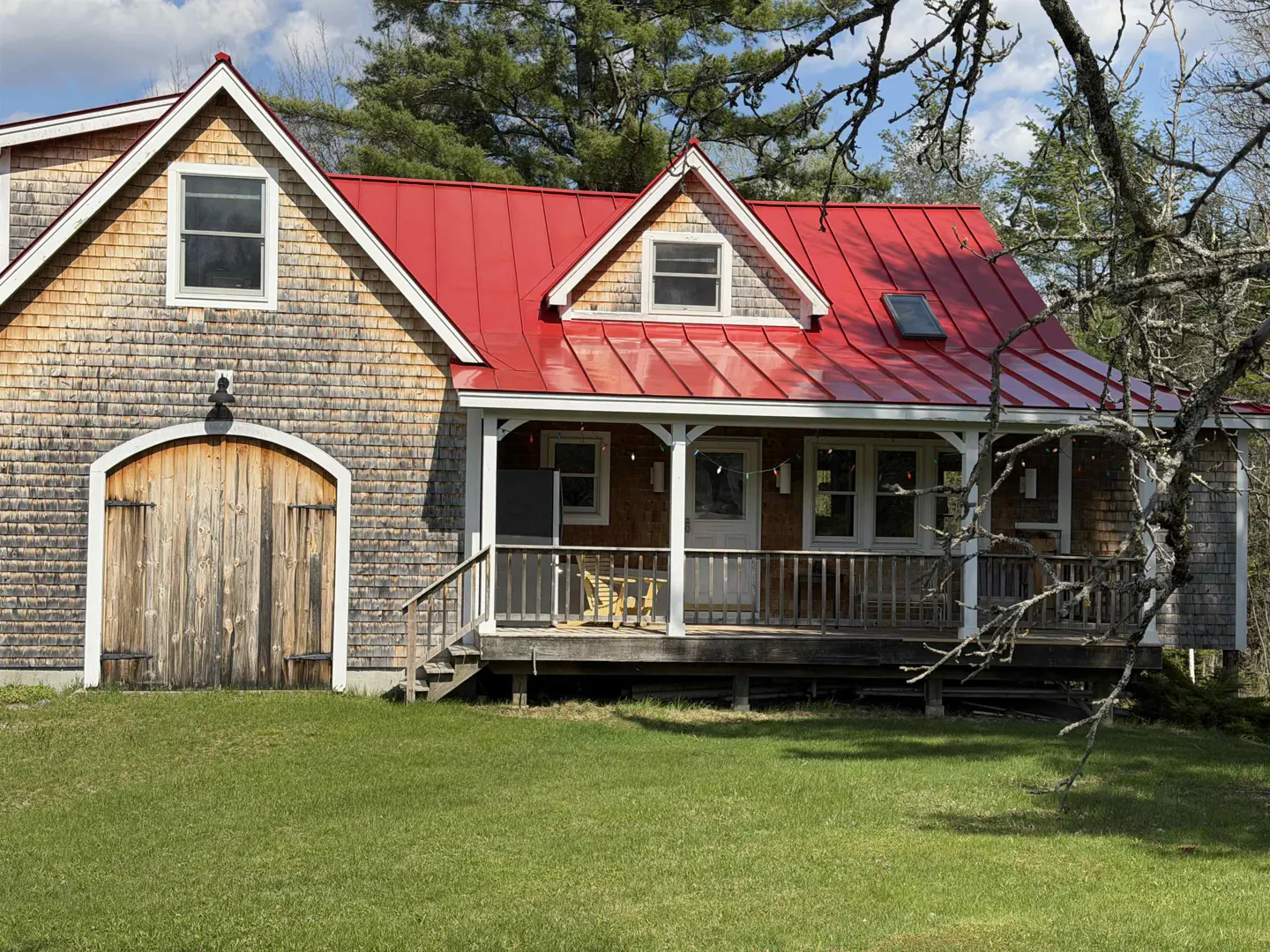 Exterior view of a shingle-sided house with a bright red roof and a wooden porch.