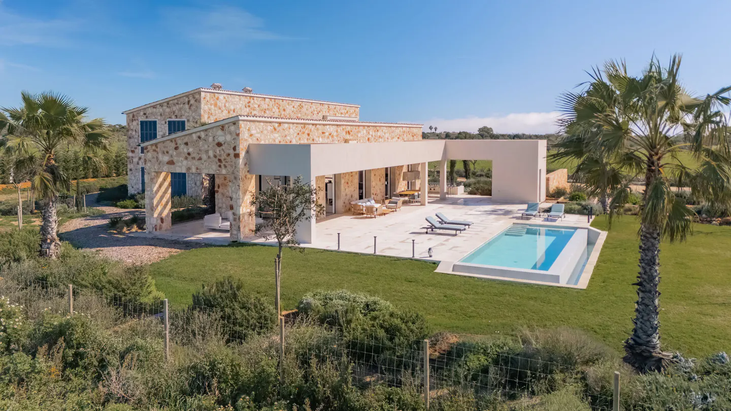Stone house with a pool. The house has a patio with lounge chairs and a dining table. Palm trees surround the property.