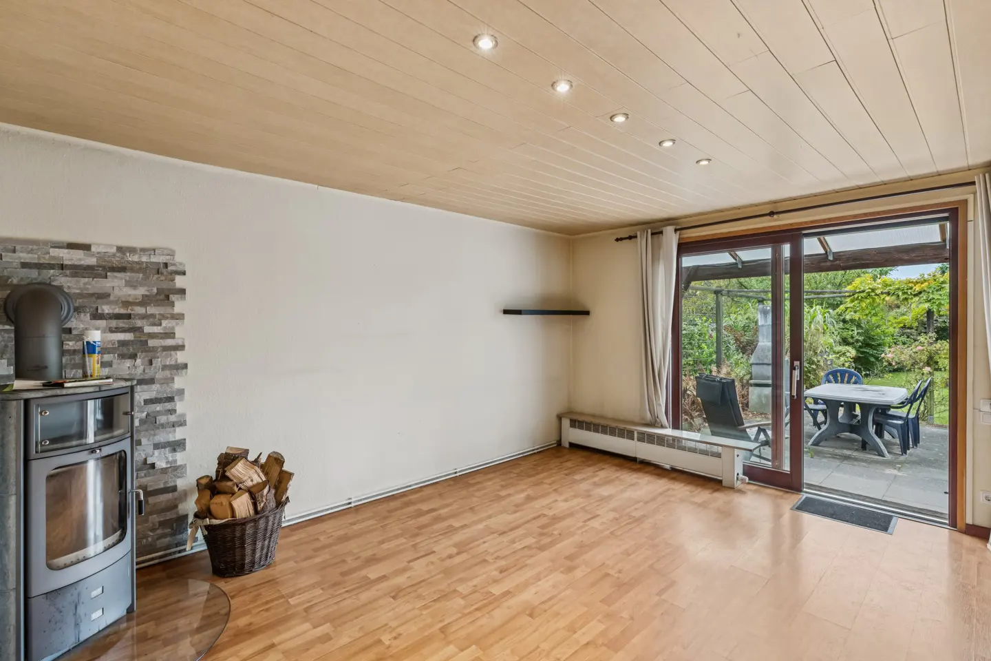 Living room with wood floors, a stone-accented wood stove, firewood basket, and sliding glass doors to a patio garden.