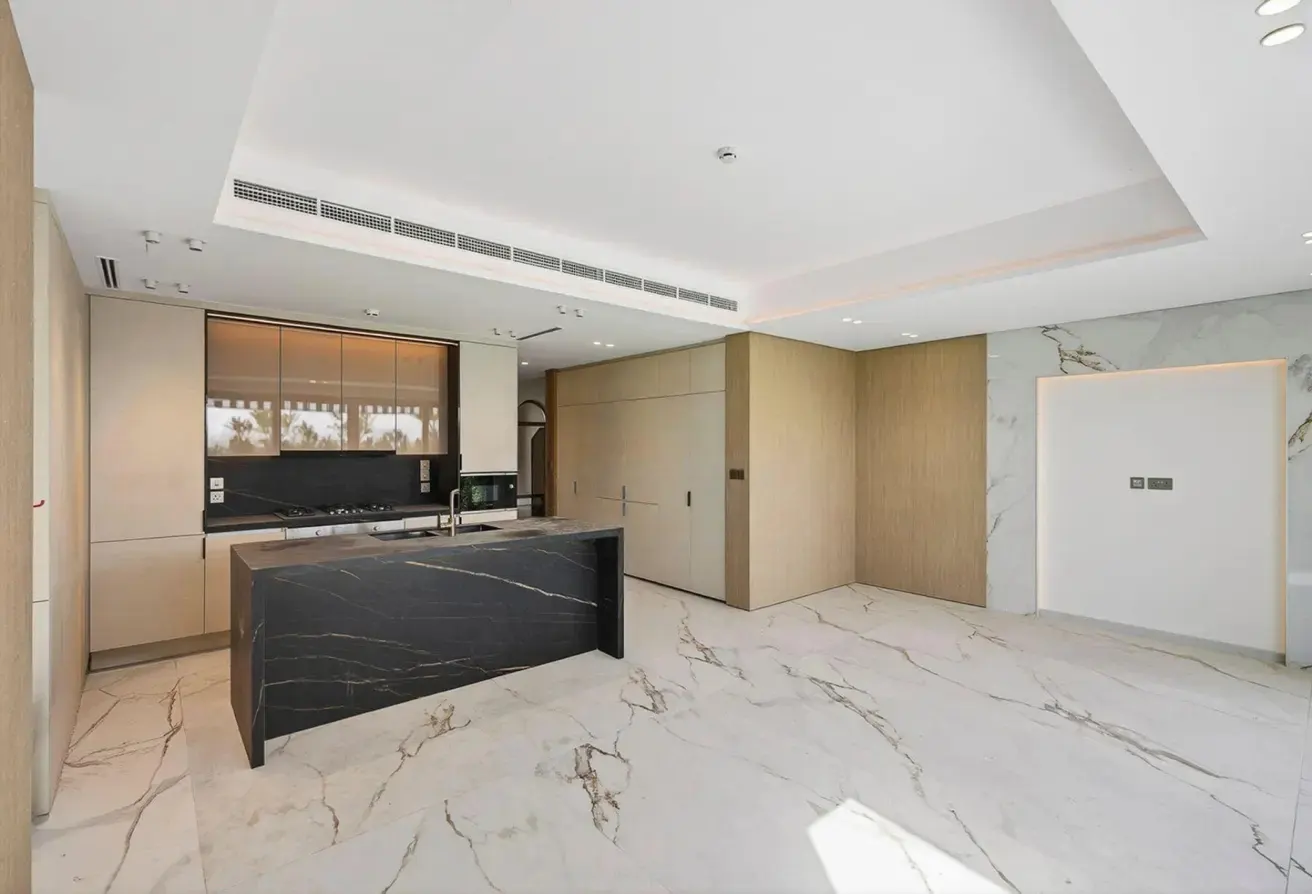 A modern kitchen with a black marble island, light wood cabinets, and white marble floors.