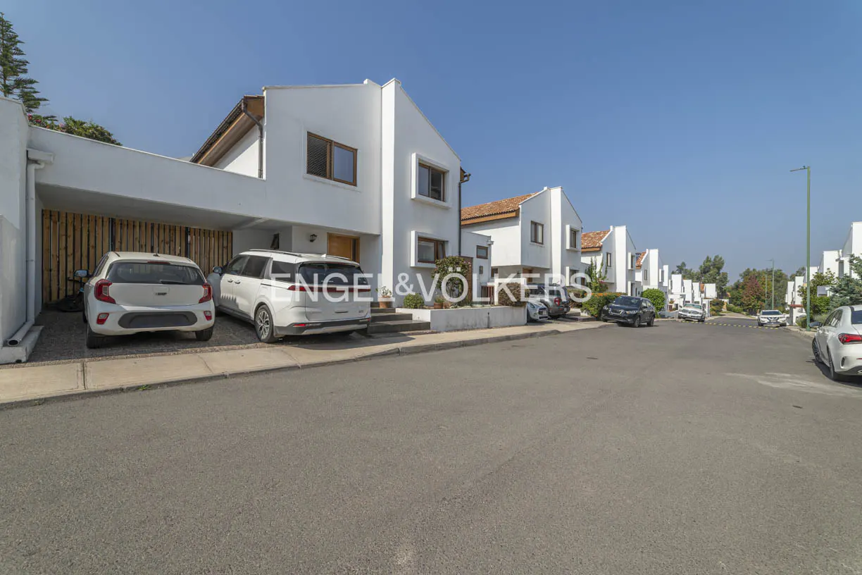 Street view of modern white townhouses with cars parked in front under a clear blue sky.
