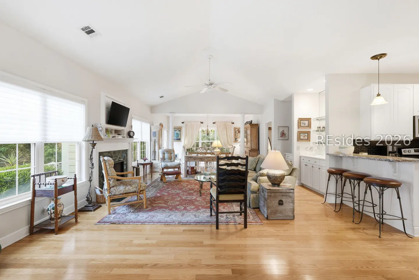 Bright, open living room with hardwood floors, a fireplace, and a kitchen bar with stools. A patterned rug adds warmth.