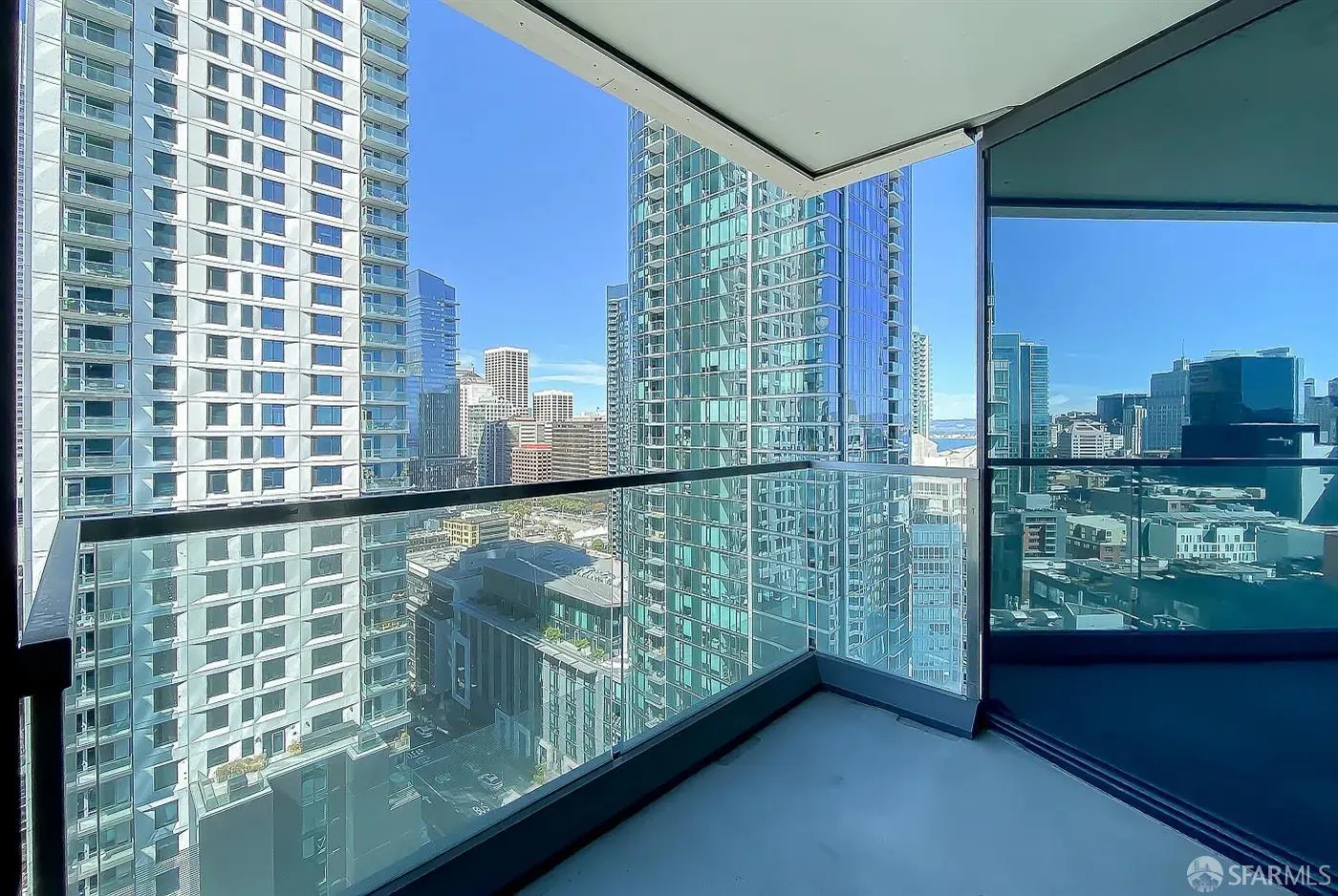 View from a condo balcony with glass railings overlooking a city skyline on a clear day. Tall buildings are visible.