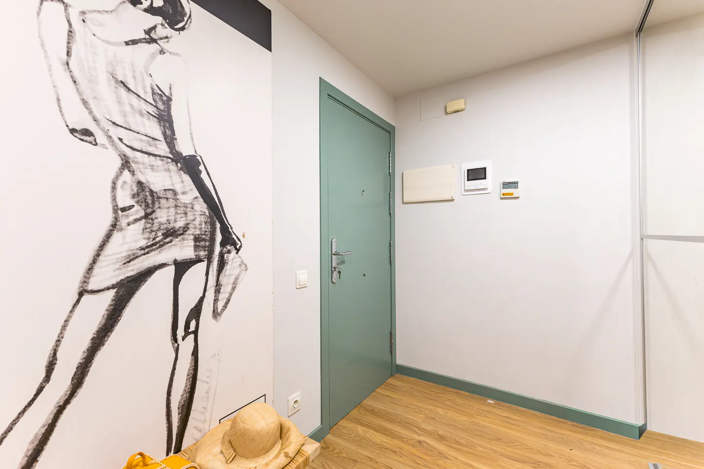 Entryway with wood floors, a light green door, and a black and white fashion illustration on the wall.