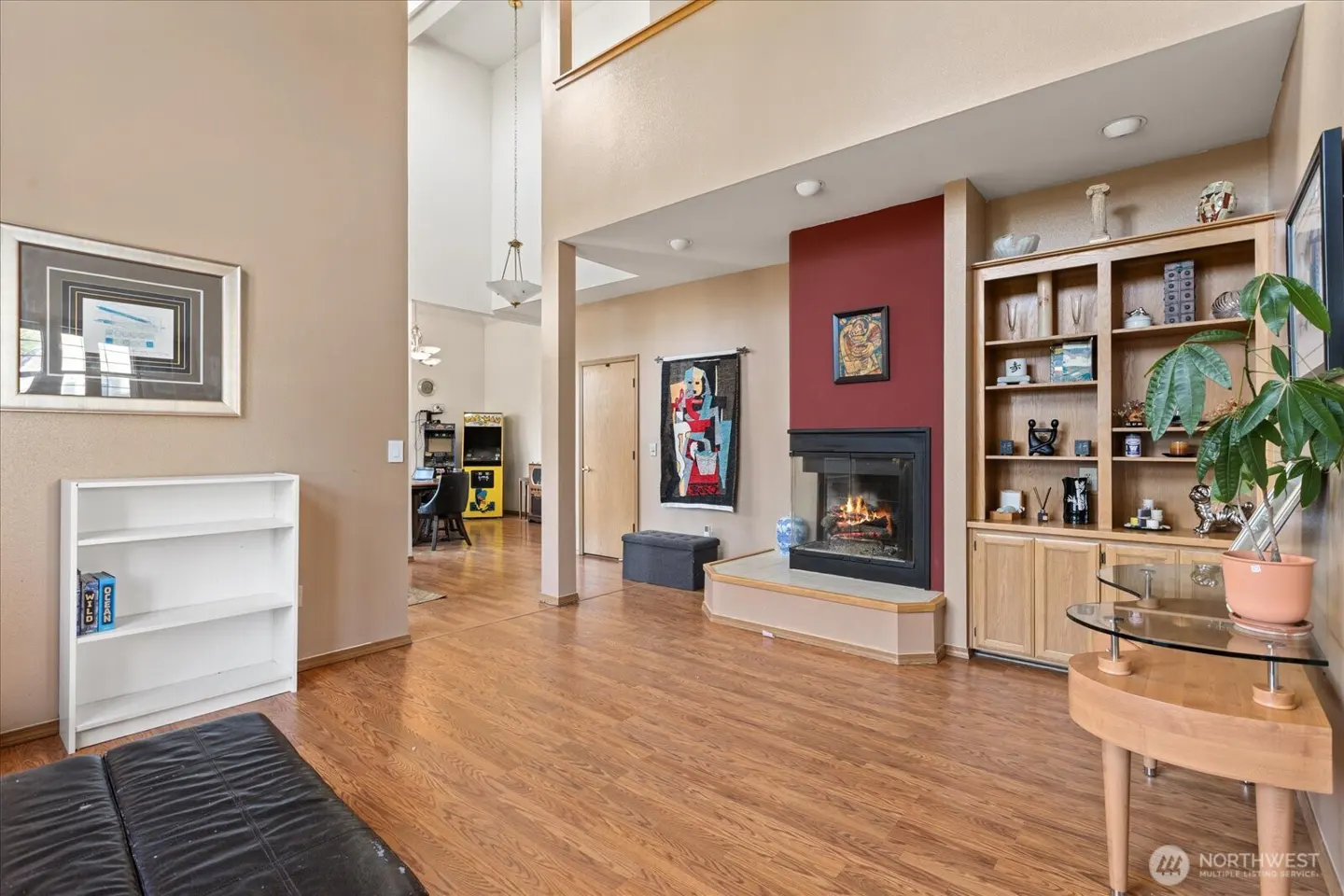 A living room with hardwood floors, a fireplace with a red accent wall, and a built-in bookshelf.