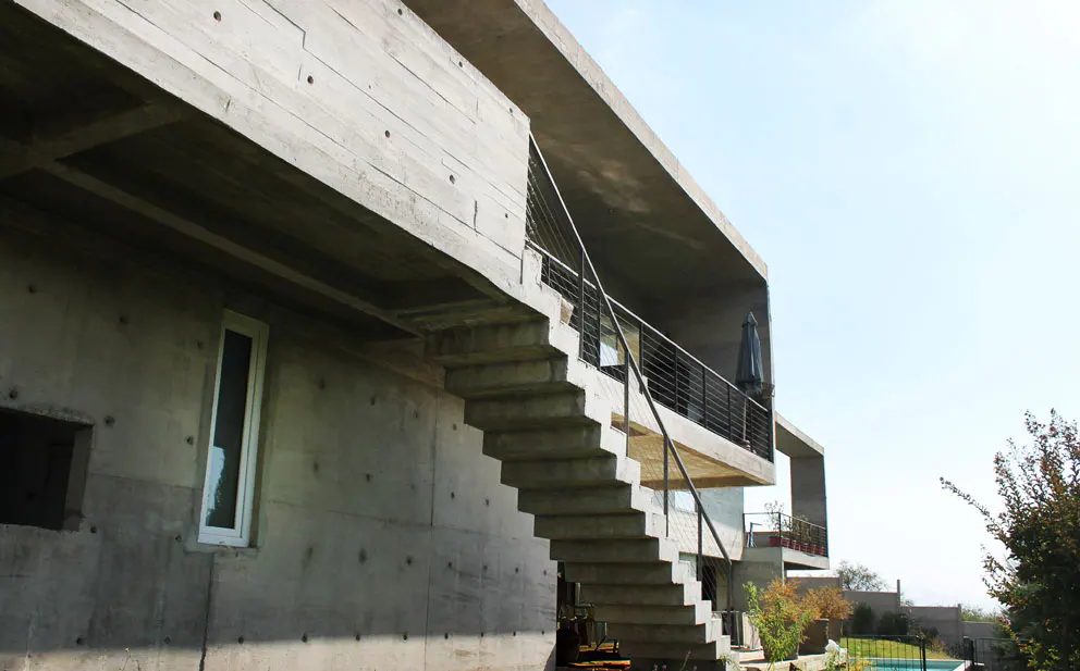 Exterior view of a modern, multi-story concrete house with outdoor stairs and a balcony.