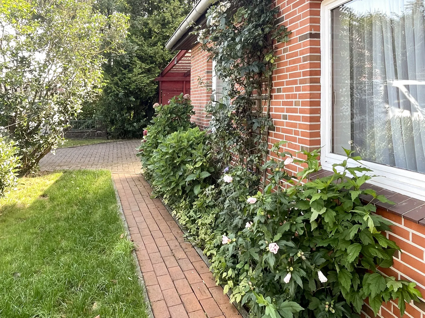 Brick house exterior with a brick walkway, green lawn, and lush landscaping. A climbing plant adorns the wall.