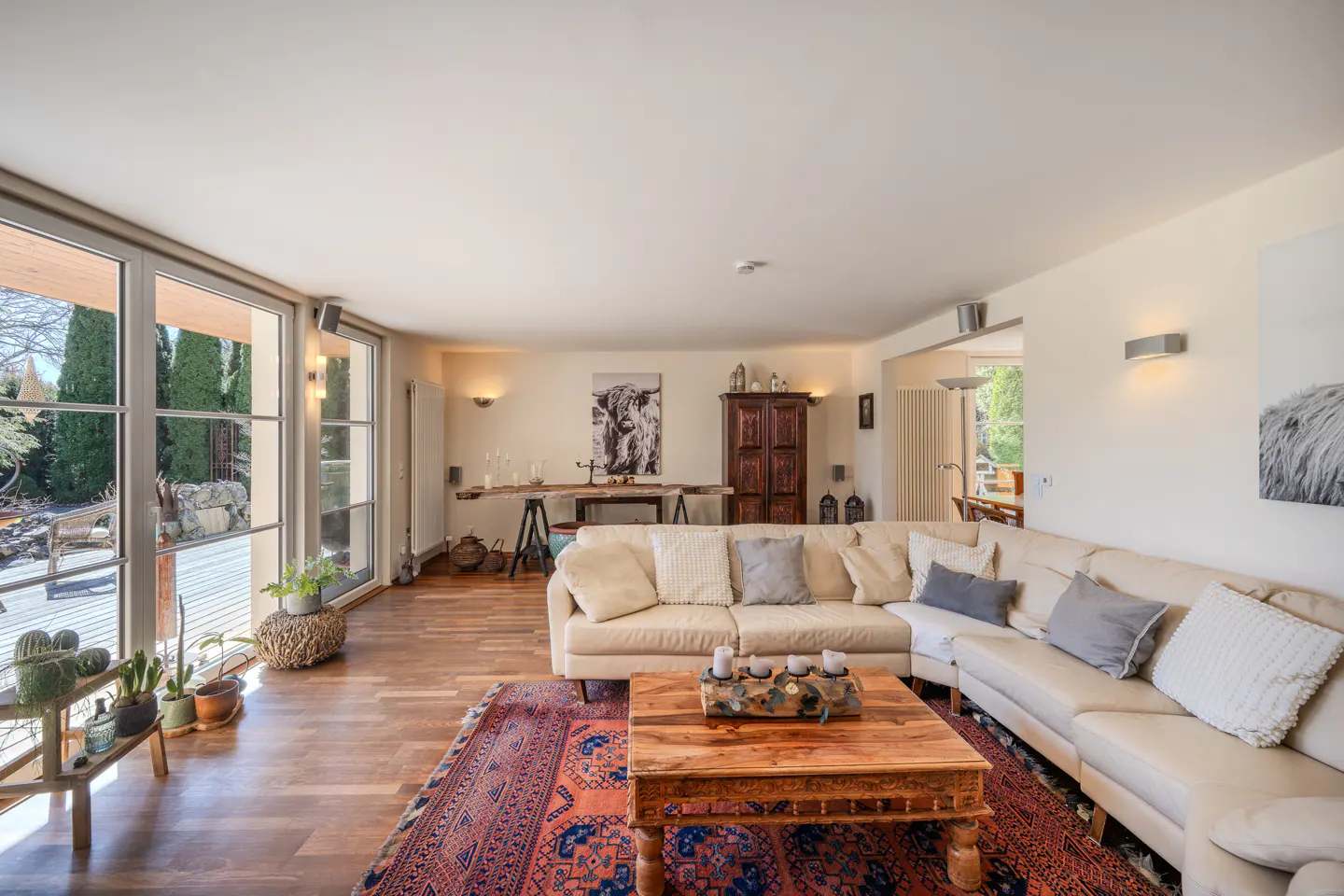 Bright living room with a large cream sectional, wooden coffee table, patterned rug, and floor-to-ceiling windows.